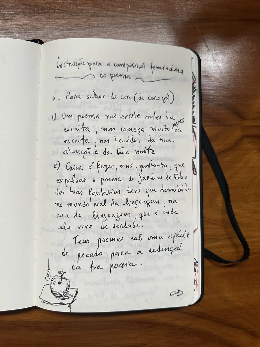 Caderno aberto sobre mesa de madeira, com uma página manuscrita a caneta e um pequeno desenho de maçã no pé da folha.